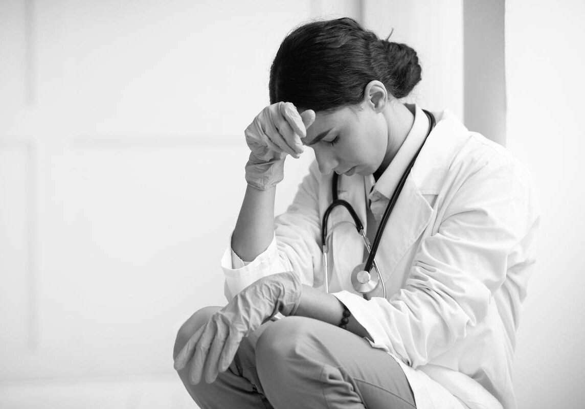 Upset female doctor sitting next to wall at clinic